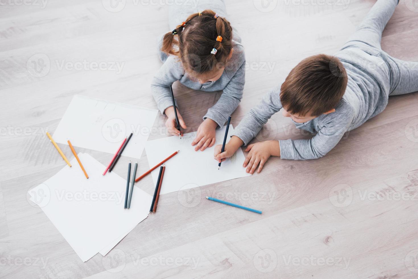 los niños se acuestan en el suelo en pijama y dibujan con lápices. lindo niño pintando con lápices foto