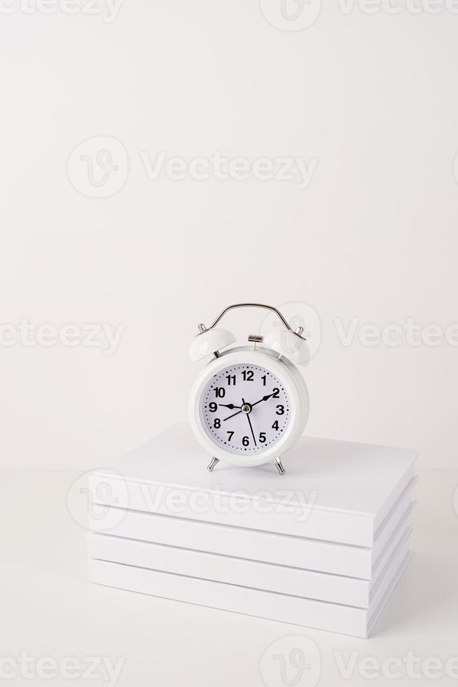 White alarm clock on stack of books, mockup design photo