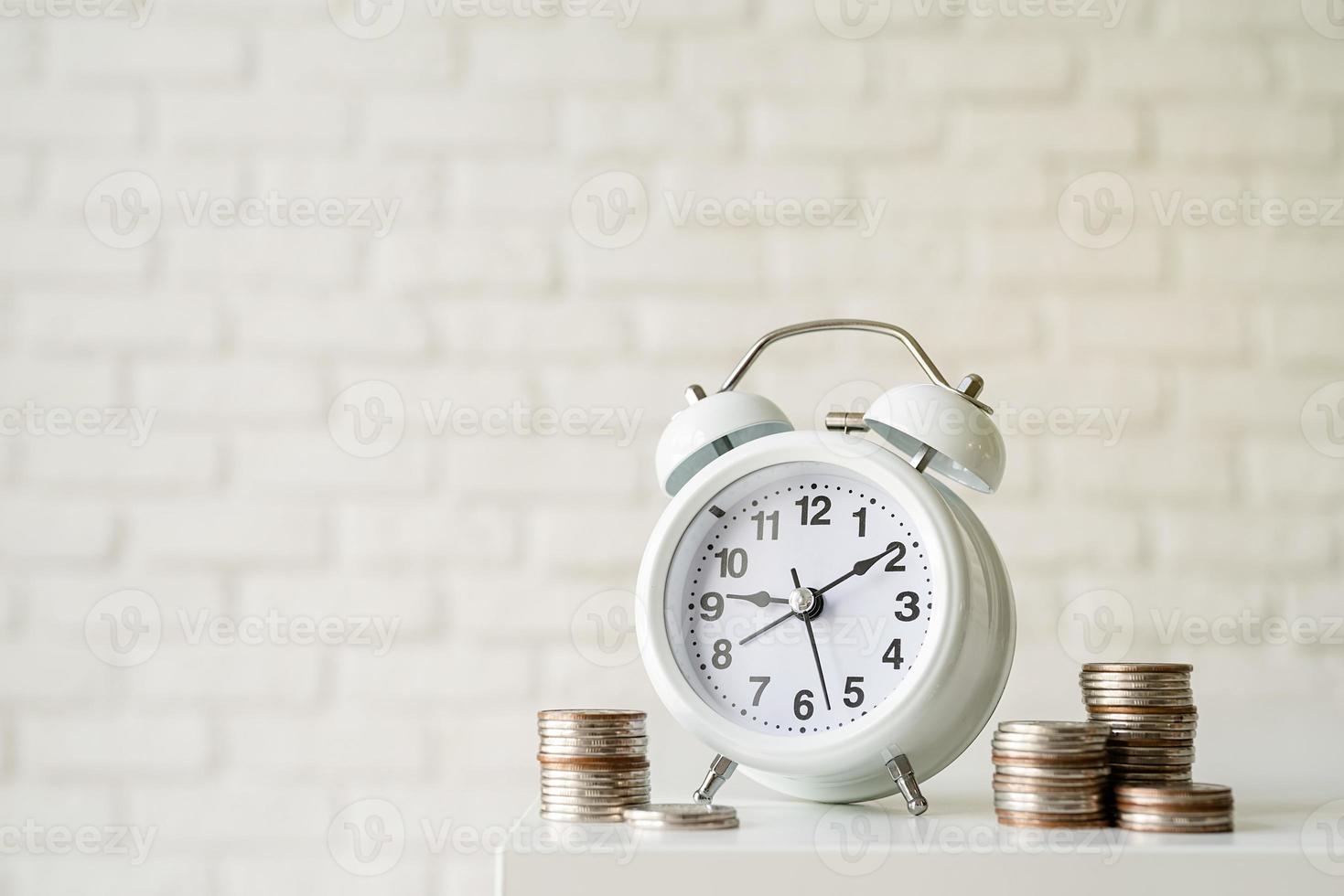 Despertador retro blanco con monedas sobre fondo de pared de ladrillo blanco foto