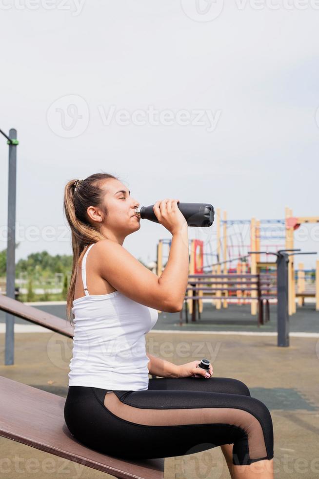 Mujer feliz trabajando en el campo de deportes en un día soleado de verano, bebiendo agua de la botella foto