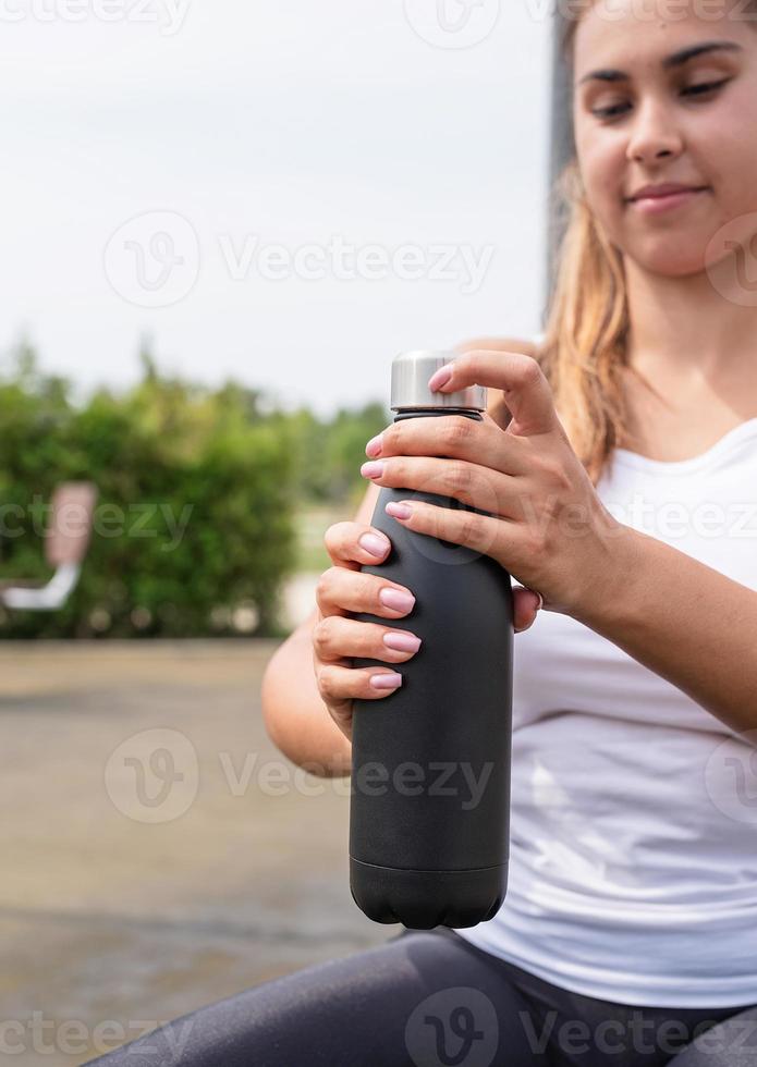 Mujer feliz trabajando en el campo de deportes en un día soleado de verano, bebiendo agua de la botella foto