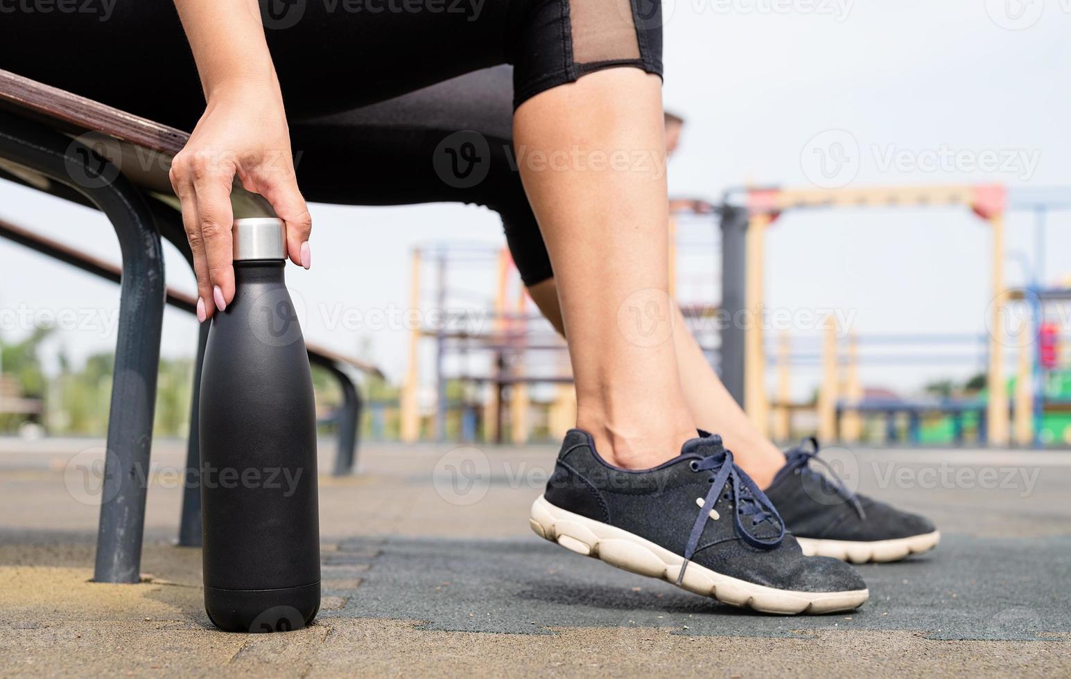 Mujer feliz trabajando en el campo de deportes en un día soleado de verano, bebiendo agua de la botella foto