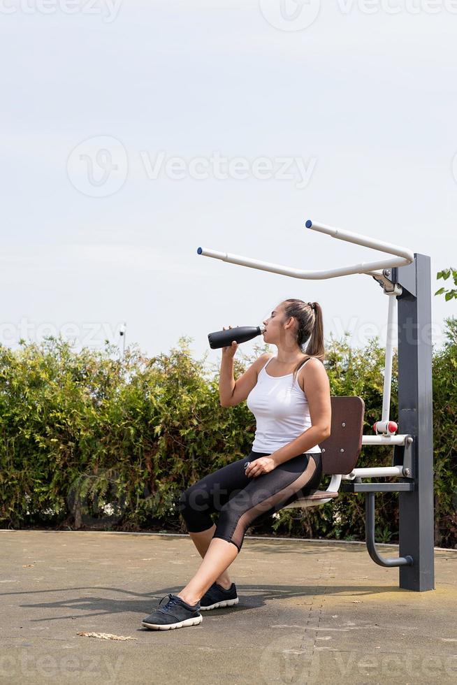 Mujer feliz trabajando en el campo de deportes en un día soleado de verano, bebiendo agua de la botella foto