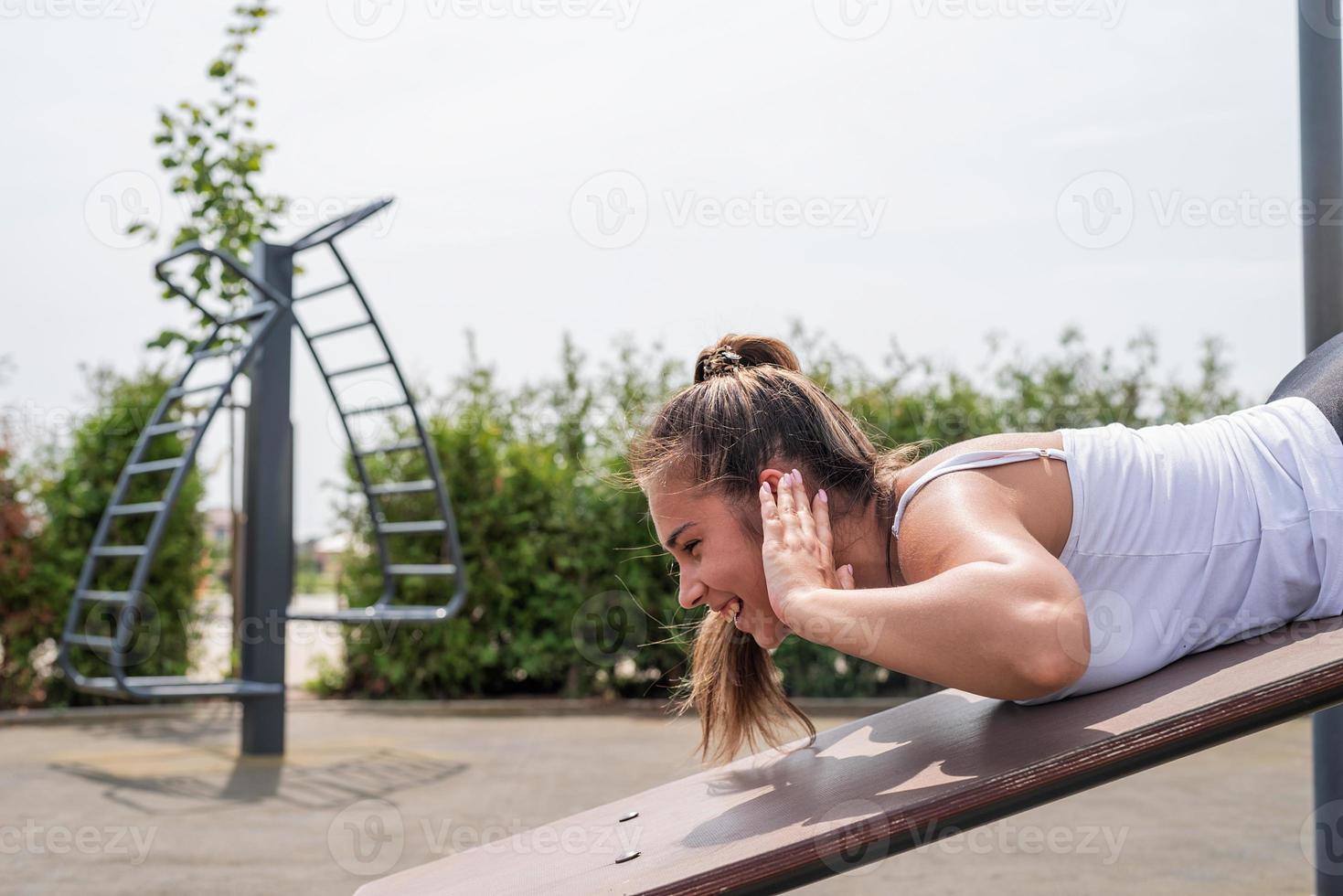 Happy woman working out on the sports ground in sunny summer day, training her back photo