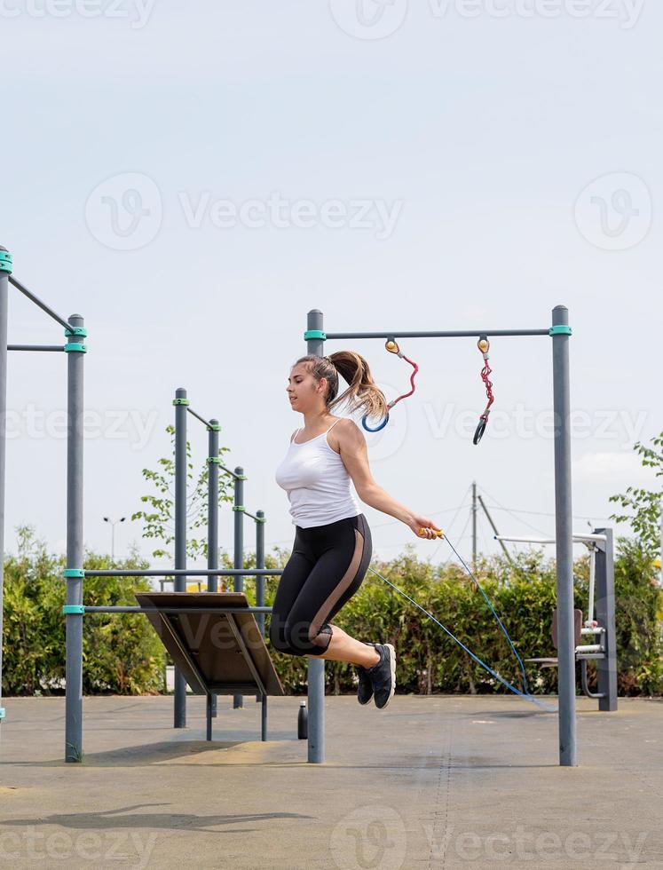 Happy woman working out on the sports ground in sunny summer day jumping rope photo