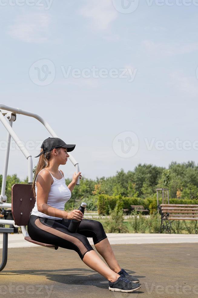 Happy woman working out on the sports ground in sunny summer day, drinking water from the bottle, having rest photo