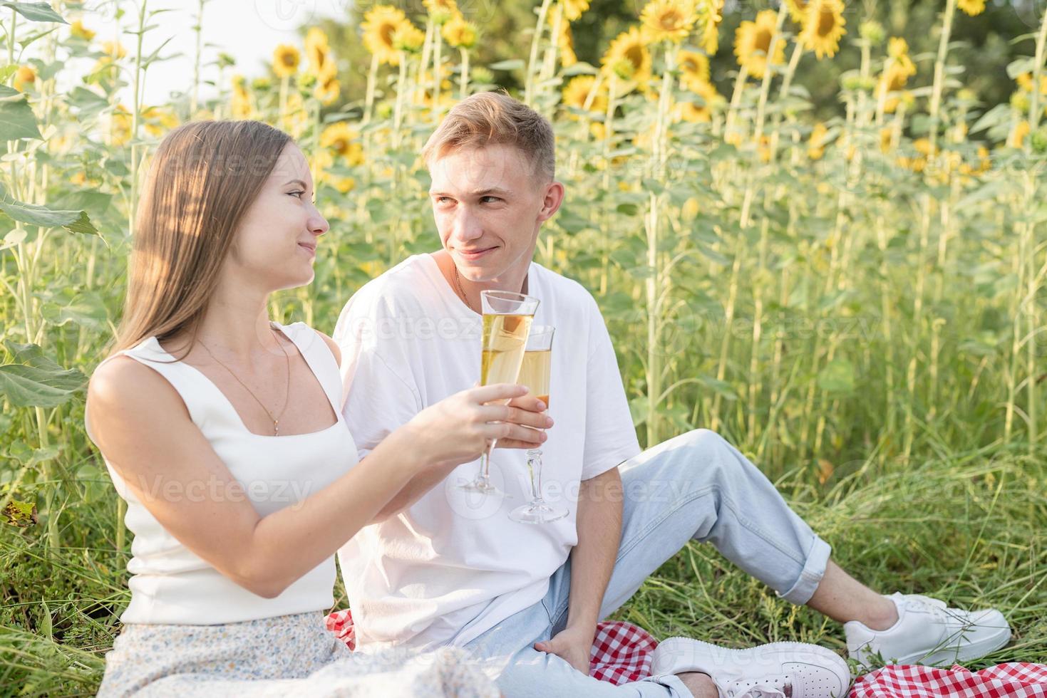 Young couple having picnic on sunflower field at sunset photo