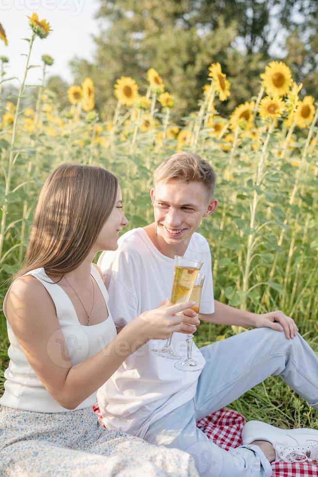 Pareja joven haciendo un picnic en el campo de girasol al atardecer foto