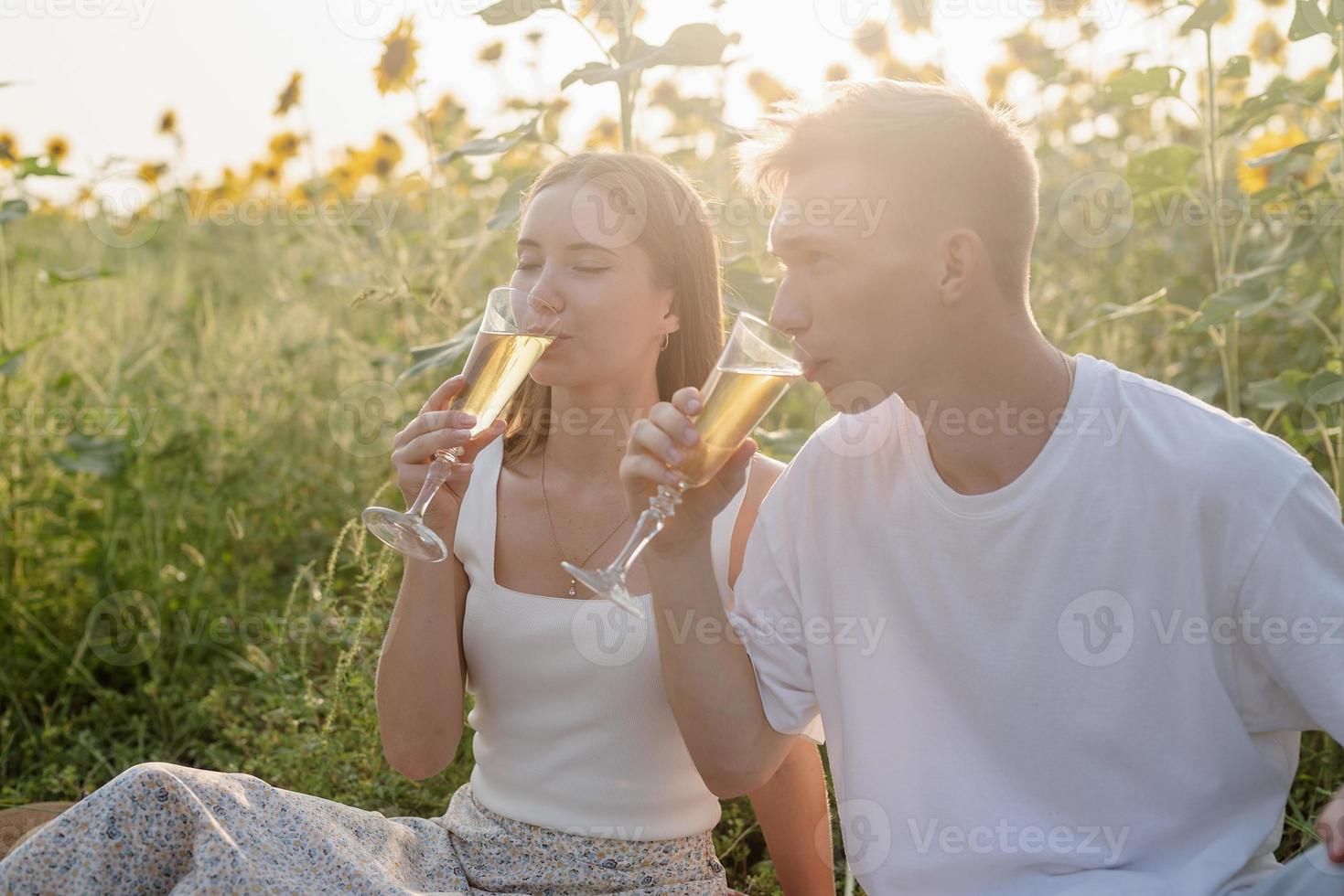 Young couple having picnic on sunflower field at sunset photo