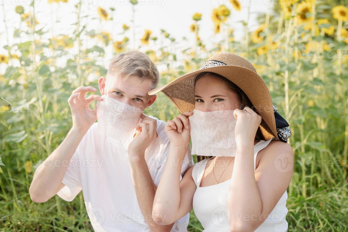 Pareja joven haciendo un picnic en el campo de girasol al atardecer, haciendo muecas foto