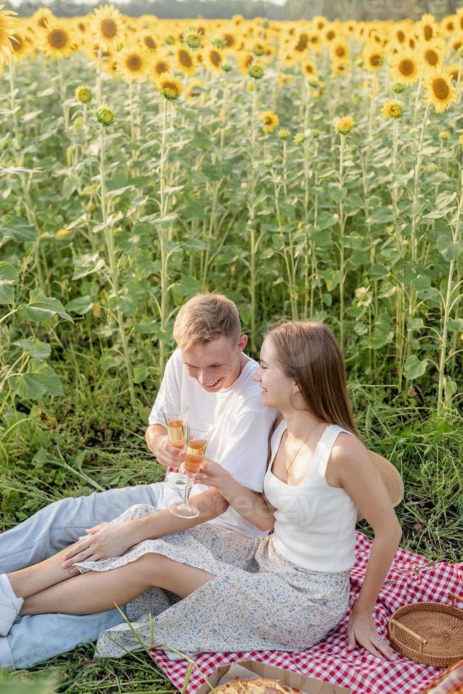 Pareja joven haciendo un picnic en el campo de girasol al atardecer foto