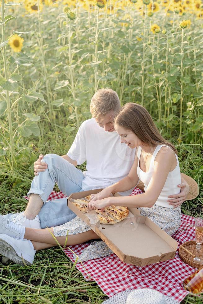 Young couple having picnic on sunflower field at sunset photo