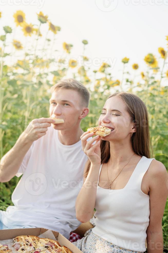 Pareja joven haciendo un picnic en el campo de girasol al atardecer foto