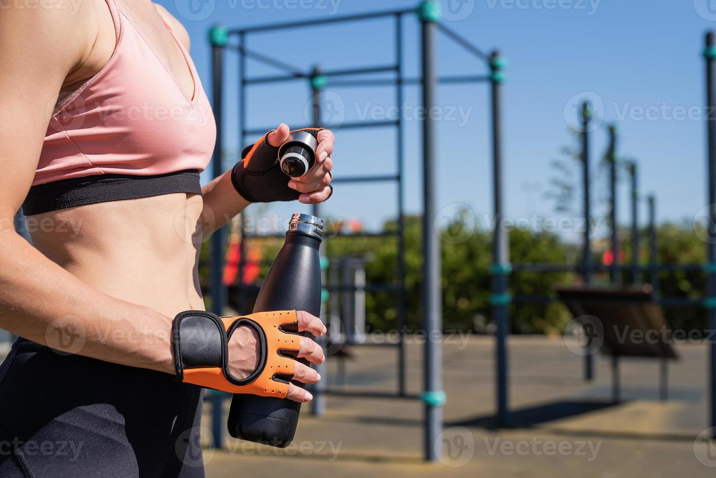 Close up of woman hands in sport gloves holding water bottle on sports ground photo