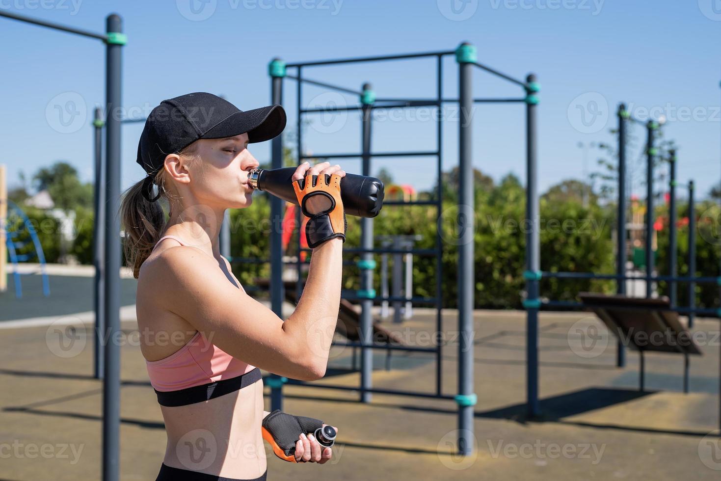 Young sportive woman in sport gloves drinking water on sport ground photo