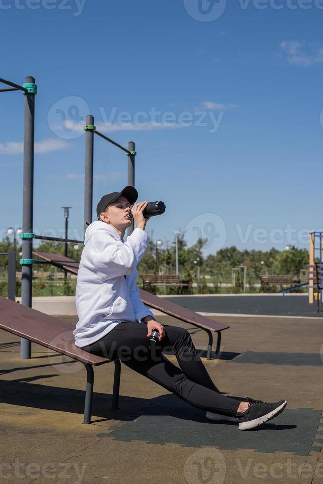 Young sportive woman in sport gloves drinking water on sport ground photo