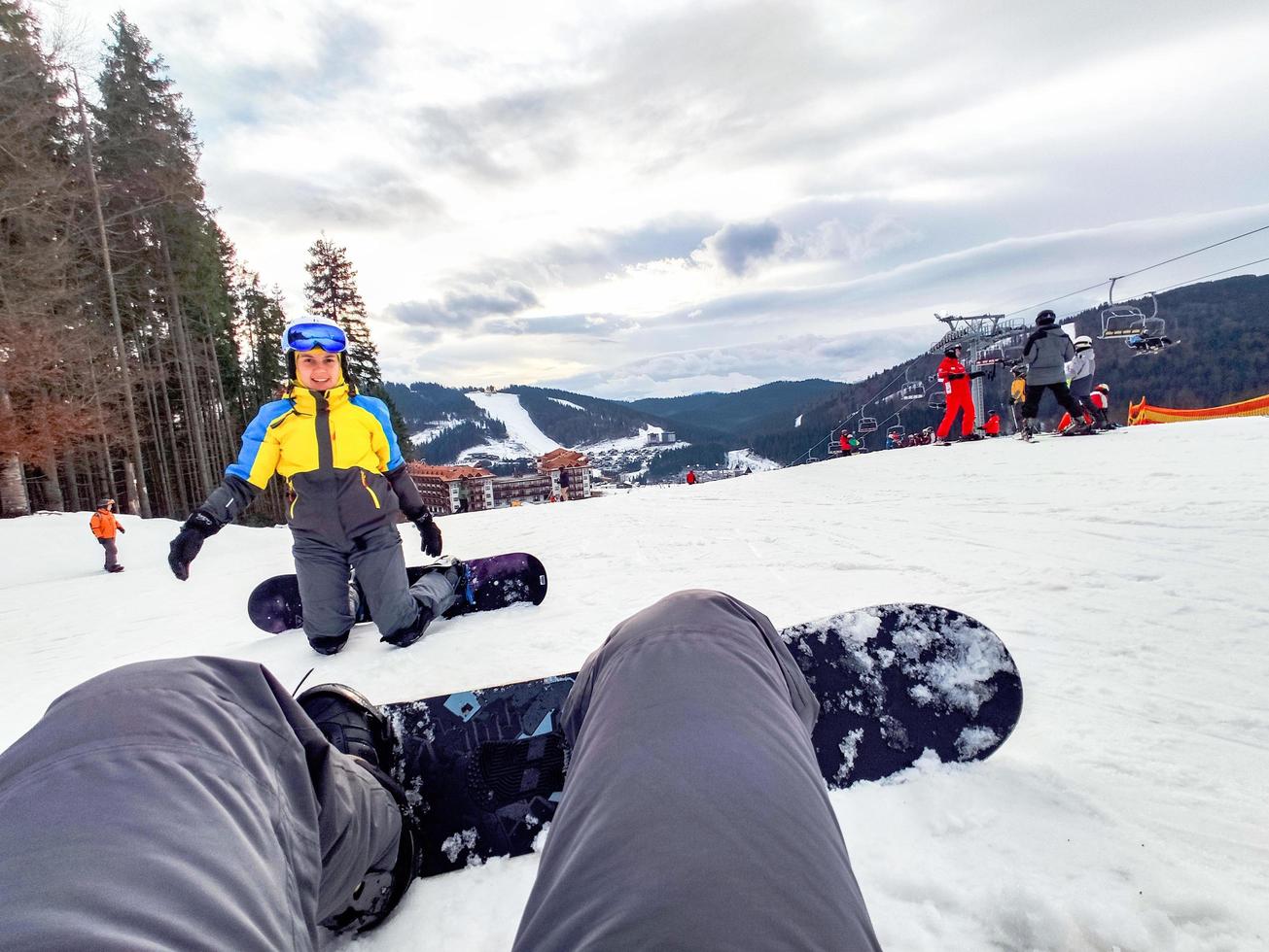 Man sitting at snowed hill with snowboard happy woman in front photo