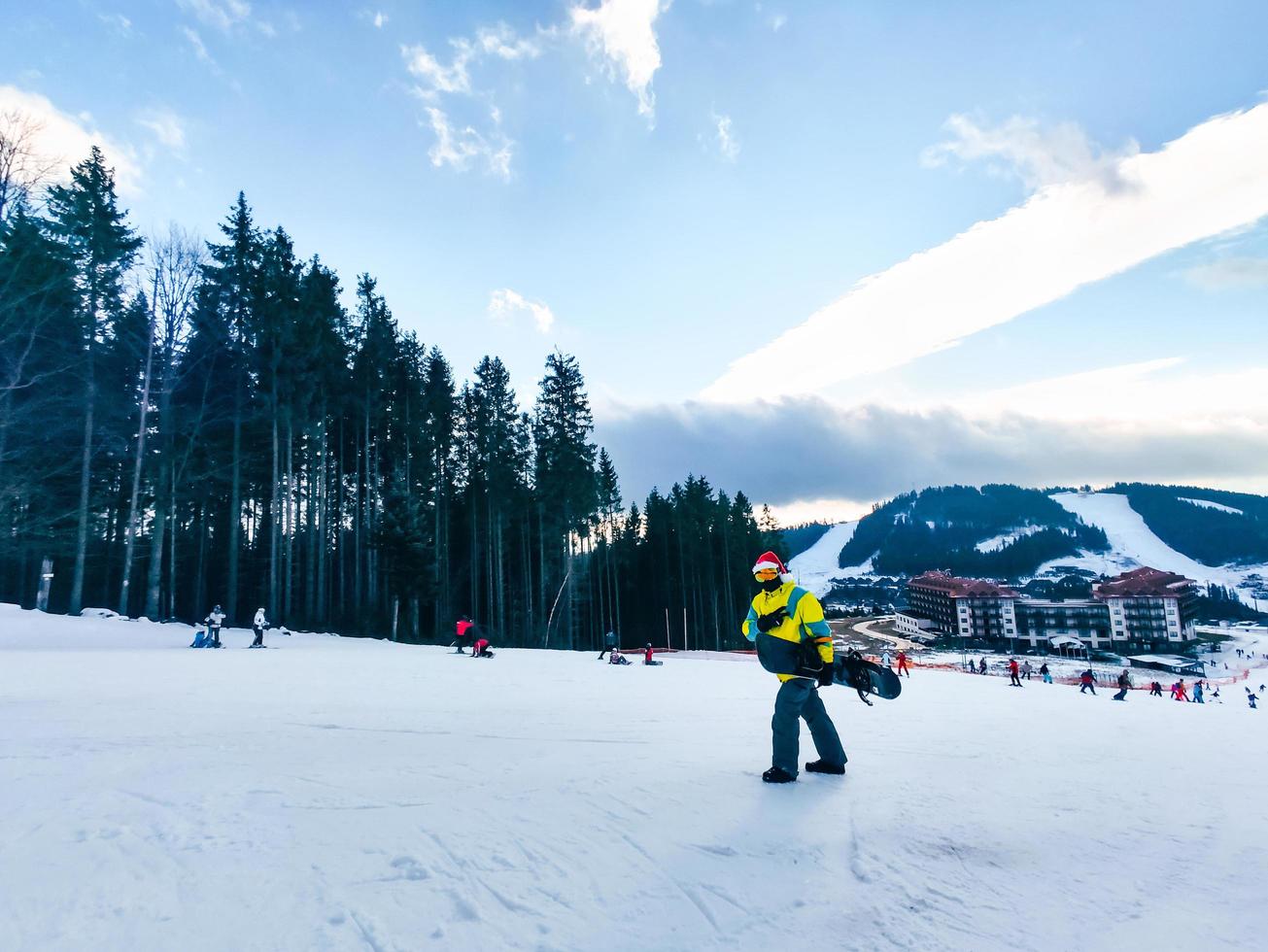 Man with snowboard in red christmas hat walking up by snowed hill photo