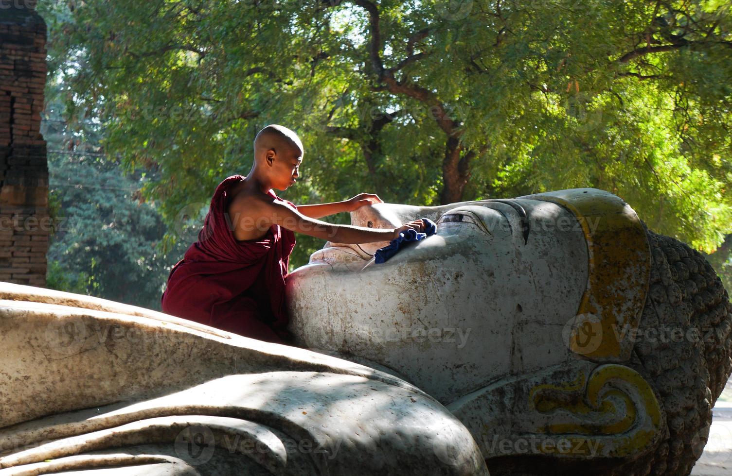 Asian novice monk clean lying Buddja statue outside temple photo