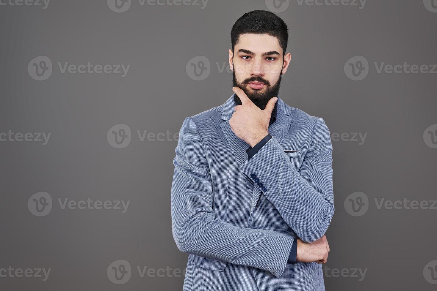 Portrait of freelancer man with beard in jacket standing against gray backdrop photo