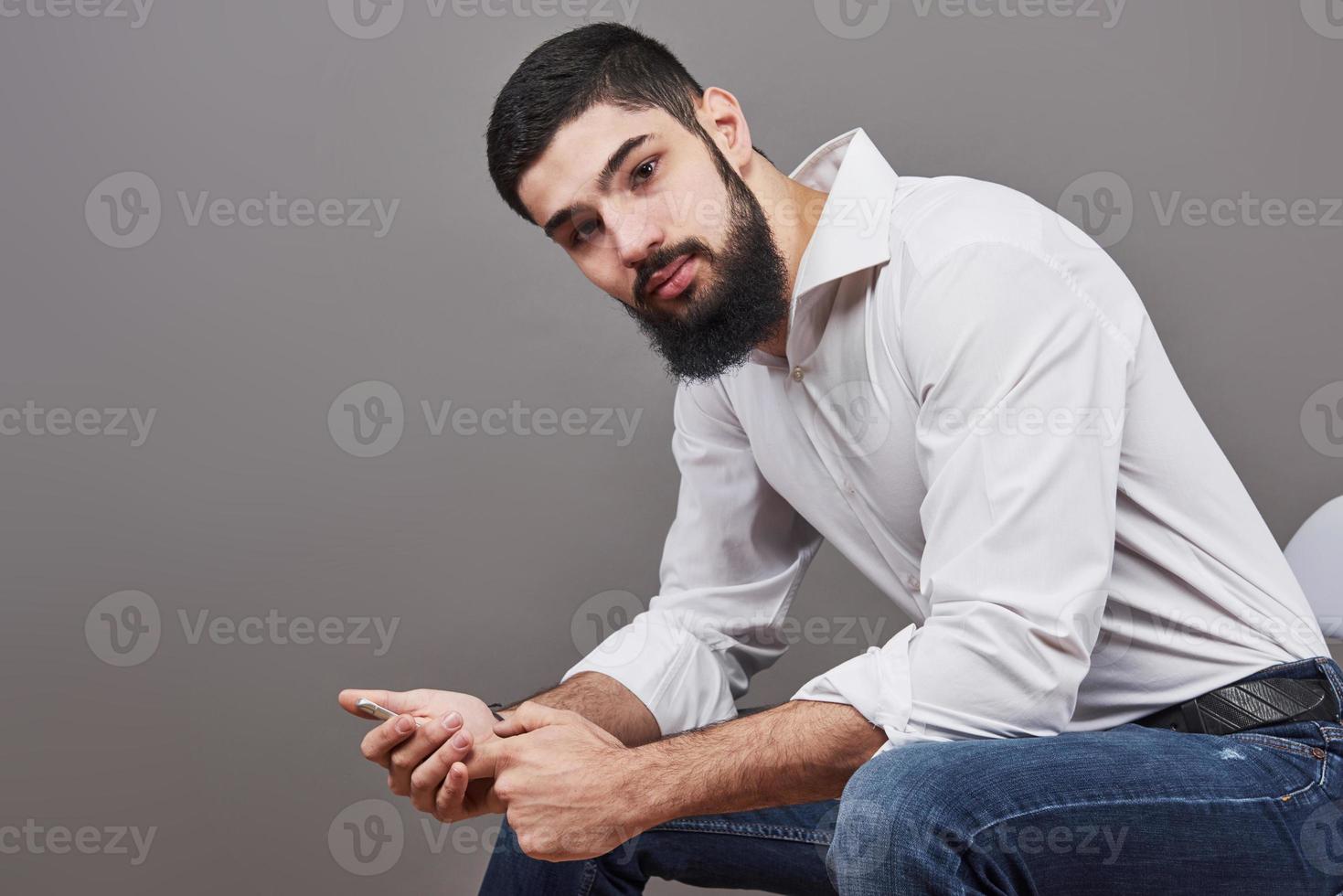 Portrait of toothy handsome bearded man sitting on a chair with phone on hands photo