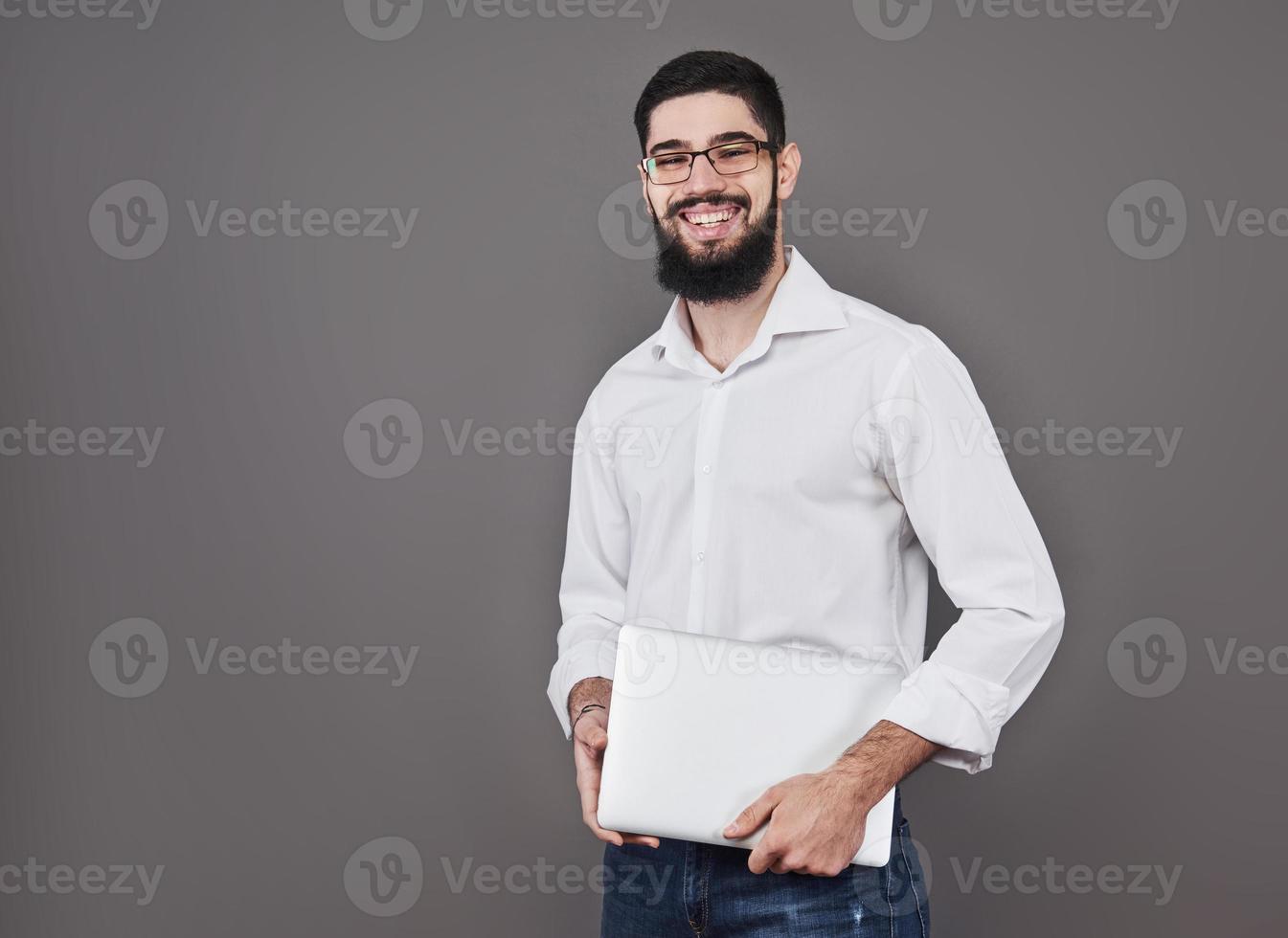 Handsome business man in glasses and suit holding laptop in hands and writing something. Side view. Isolated gray background photo