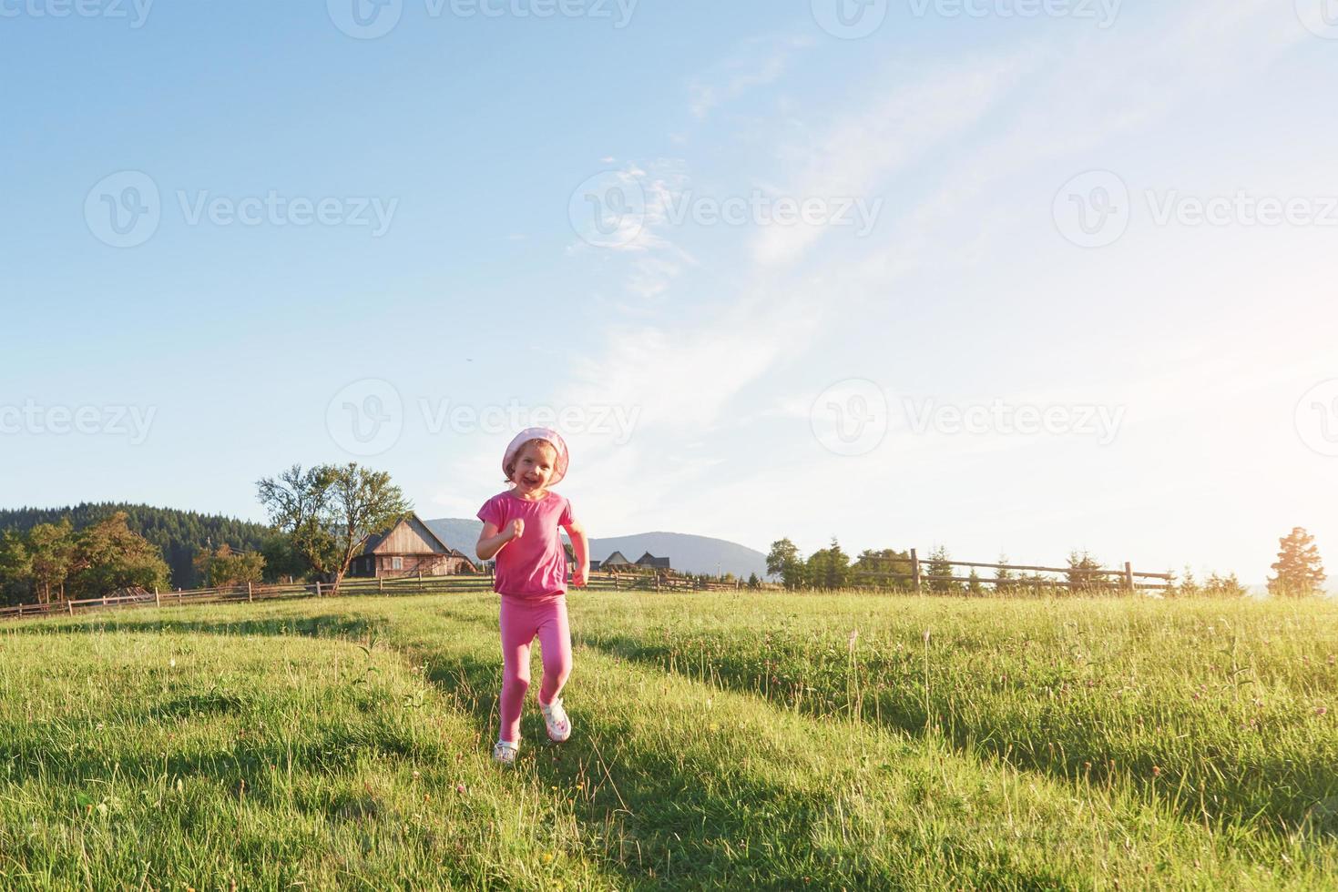 Cute happy little baby girl play outdoors in the early morning in the lawn and admiring mountains view. Copy space for your text photo