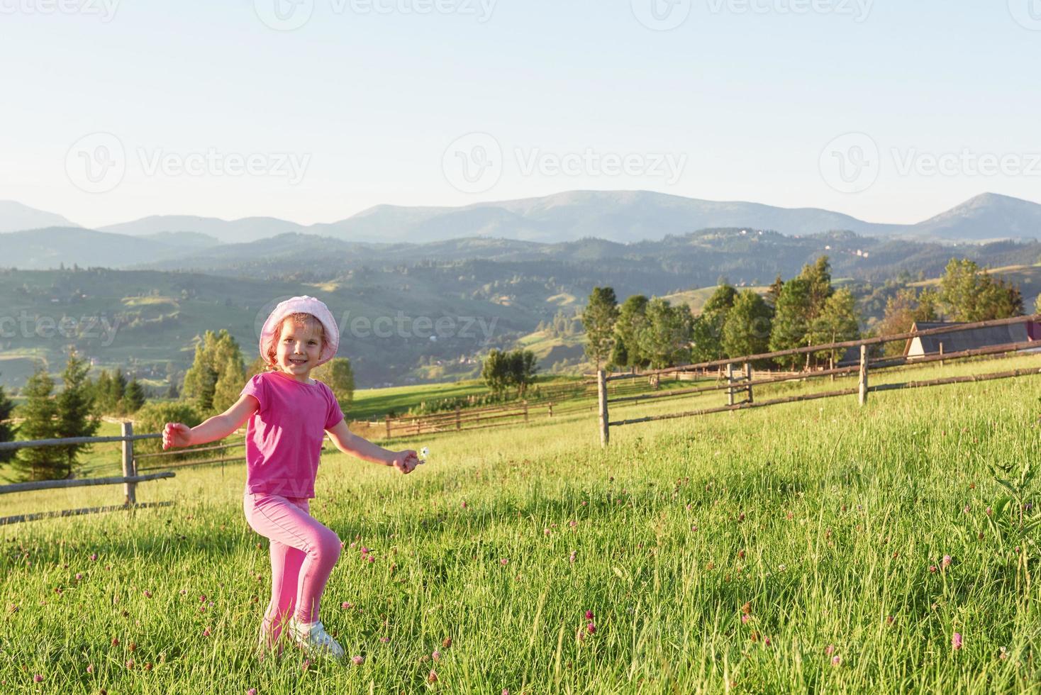 Linda niña feliz juega al aire libre en el césped y admira la vista de las montañas. copia espacio para tu texto foto