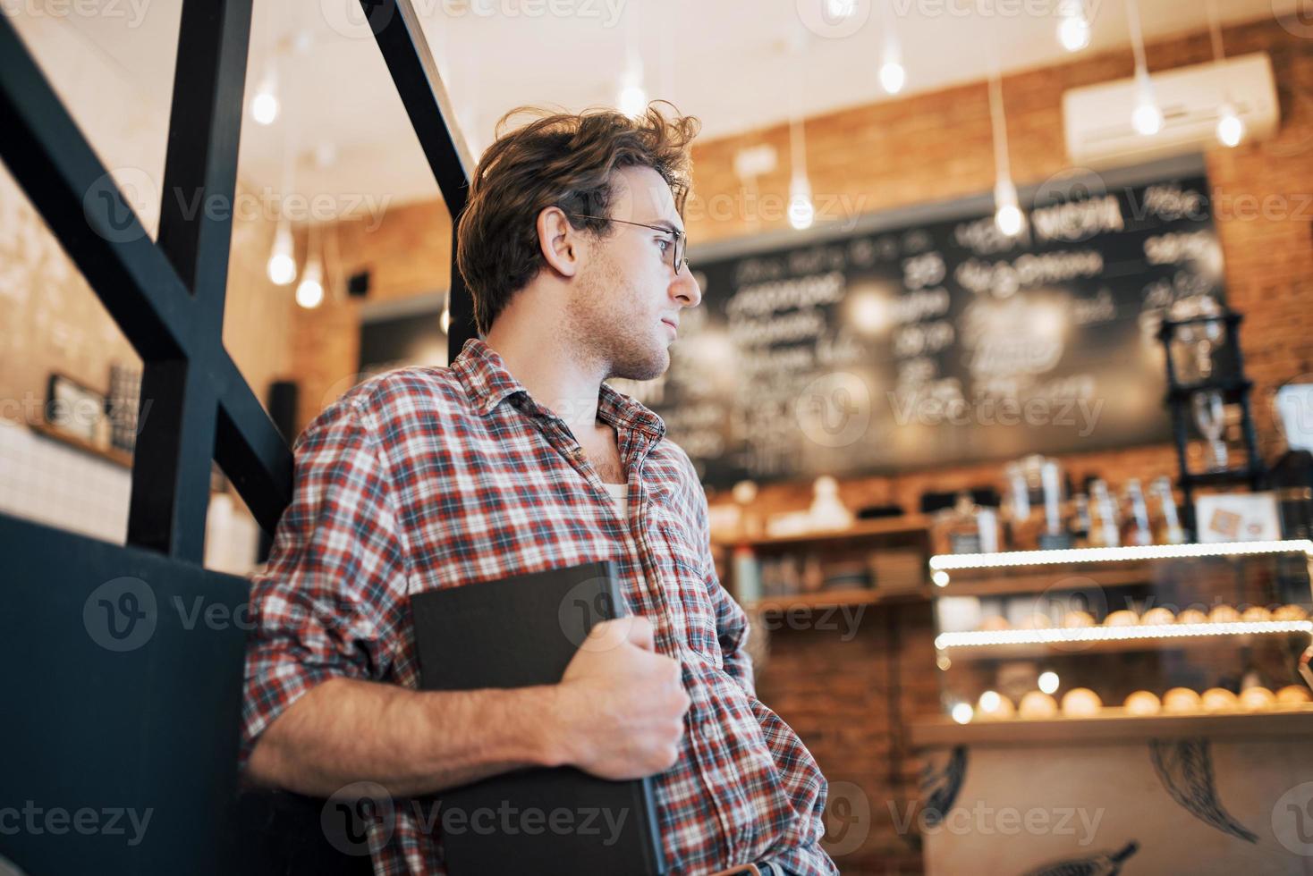 Joven talentoso en camisa casual dibujo boceto en cuaderno disfrutando de tiempo libre en la cafetería.Estudiante calificado escribiendo tareas en el bloc de notas sentado en coworking foto