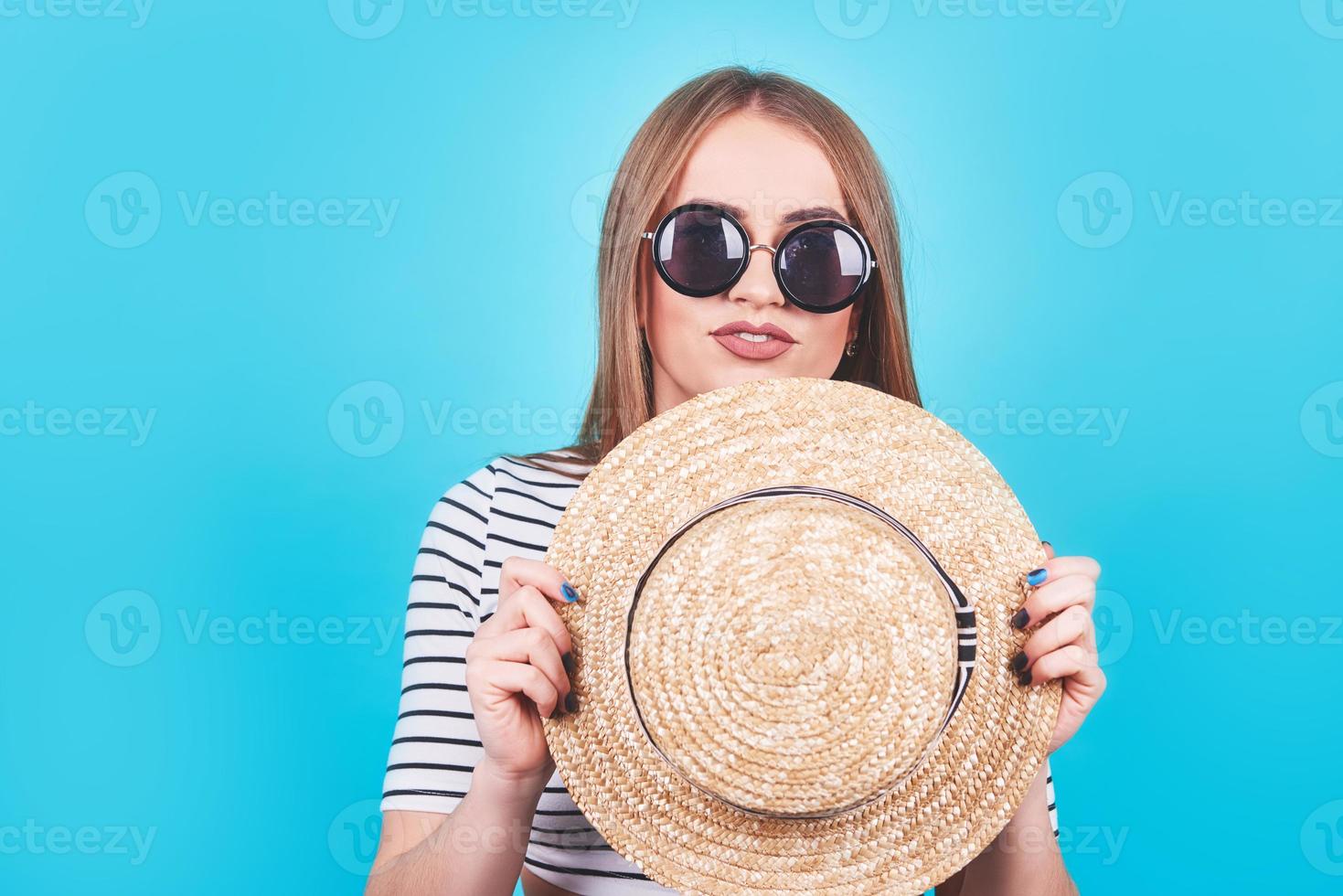 chica atractiva con rayas blancas y negras, sombrero, gafas de sol, boca abierta emocionalmente sobre un fondo azul brillante con un cuerpo perfecto. aislado. tiro del estudio foto