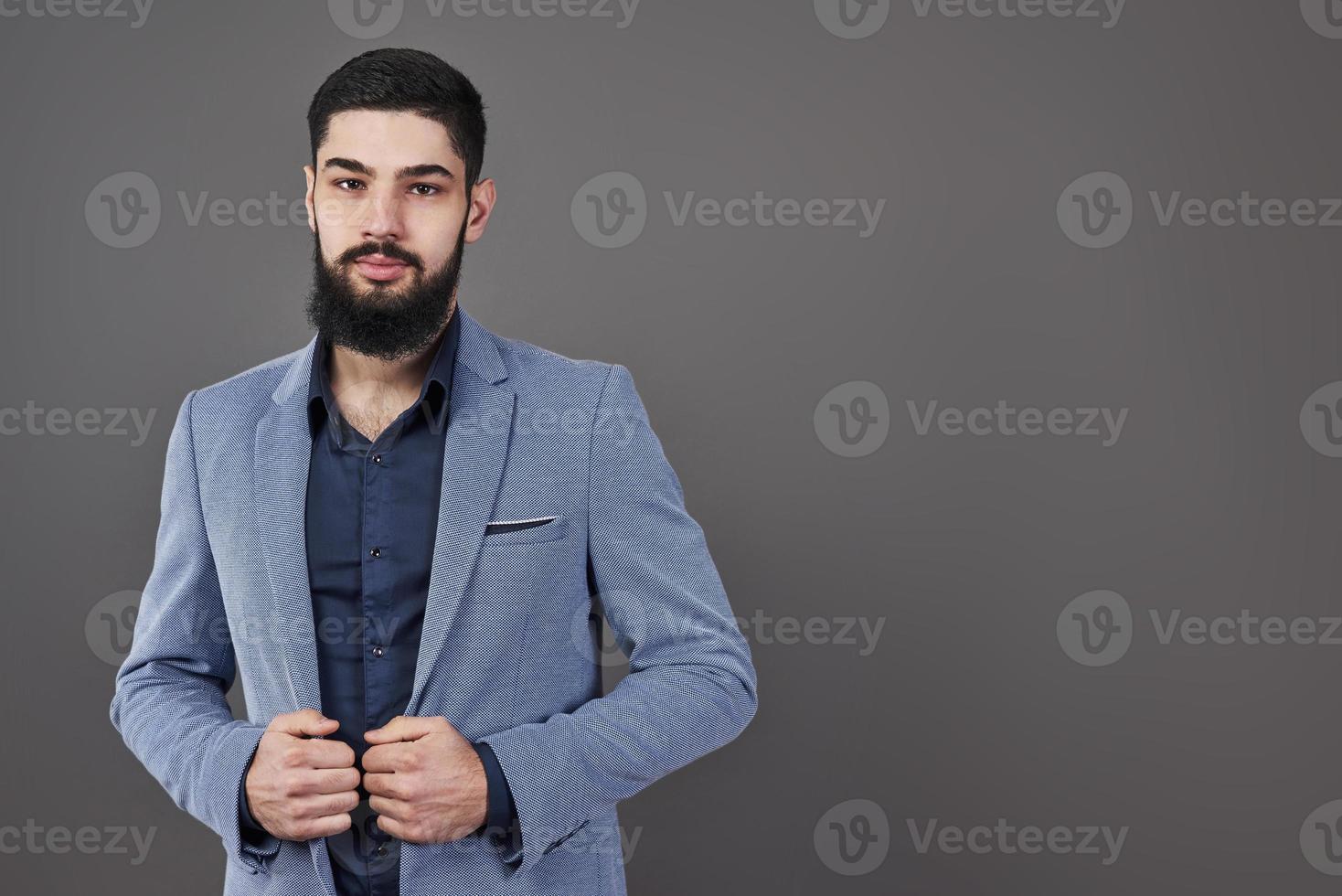 Portrait of freelancer man with beard in jacket standing against gray backdrop photo