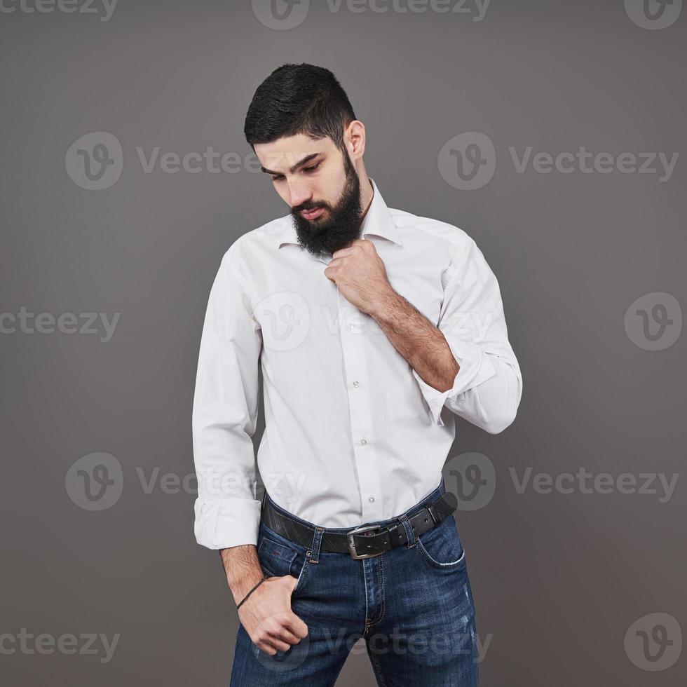 Handsome young bearded man is looking away while standing against gray background photo