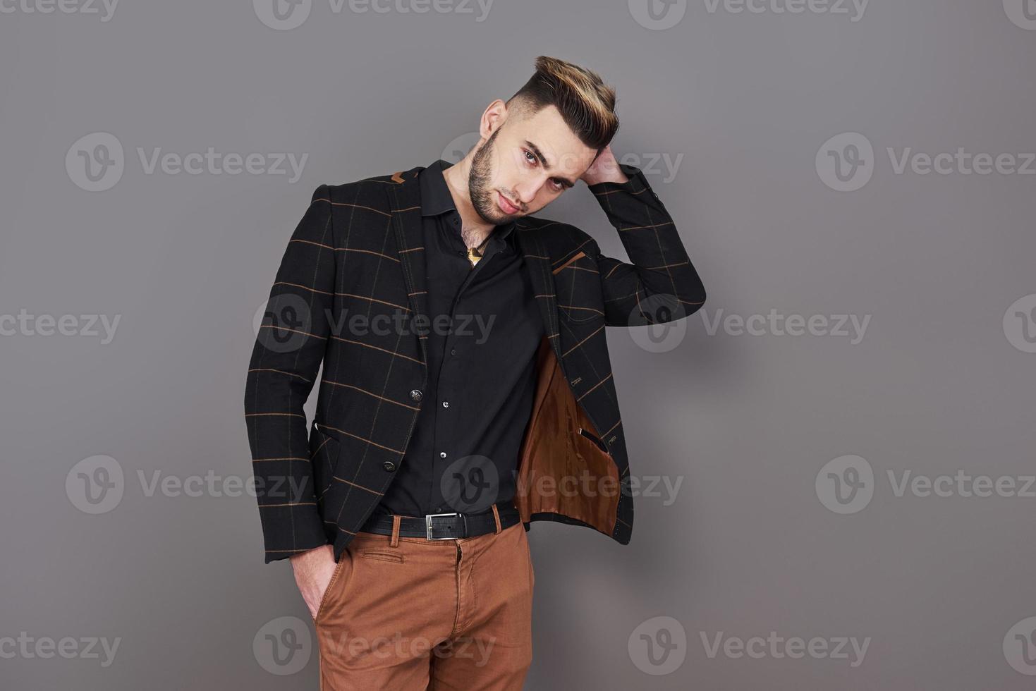 Exitoso joven empresario con un traje marrón con una hermosa sonrisa genuina posando sobre un fondo gris oscuro con espacio de copia foto