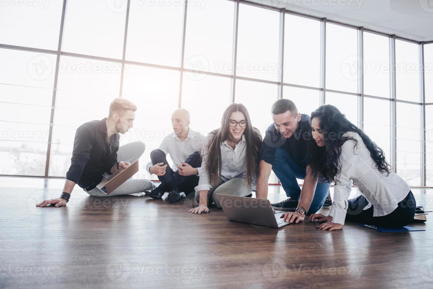 jóvenes creativos en la oficina moderna. grupo de jóvenes empresarios están trabajando junto con la computadora portátil. autónomos sentados en el suelo. logro corporativo de cooperación. concepto de trabajo en equipo foto