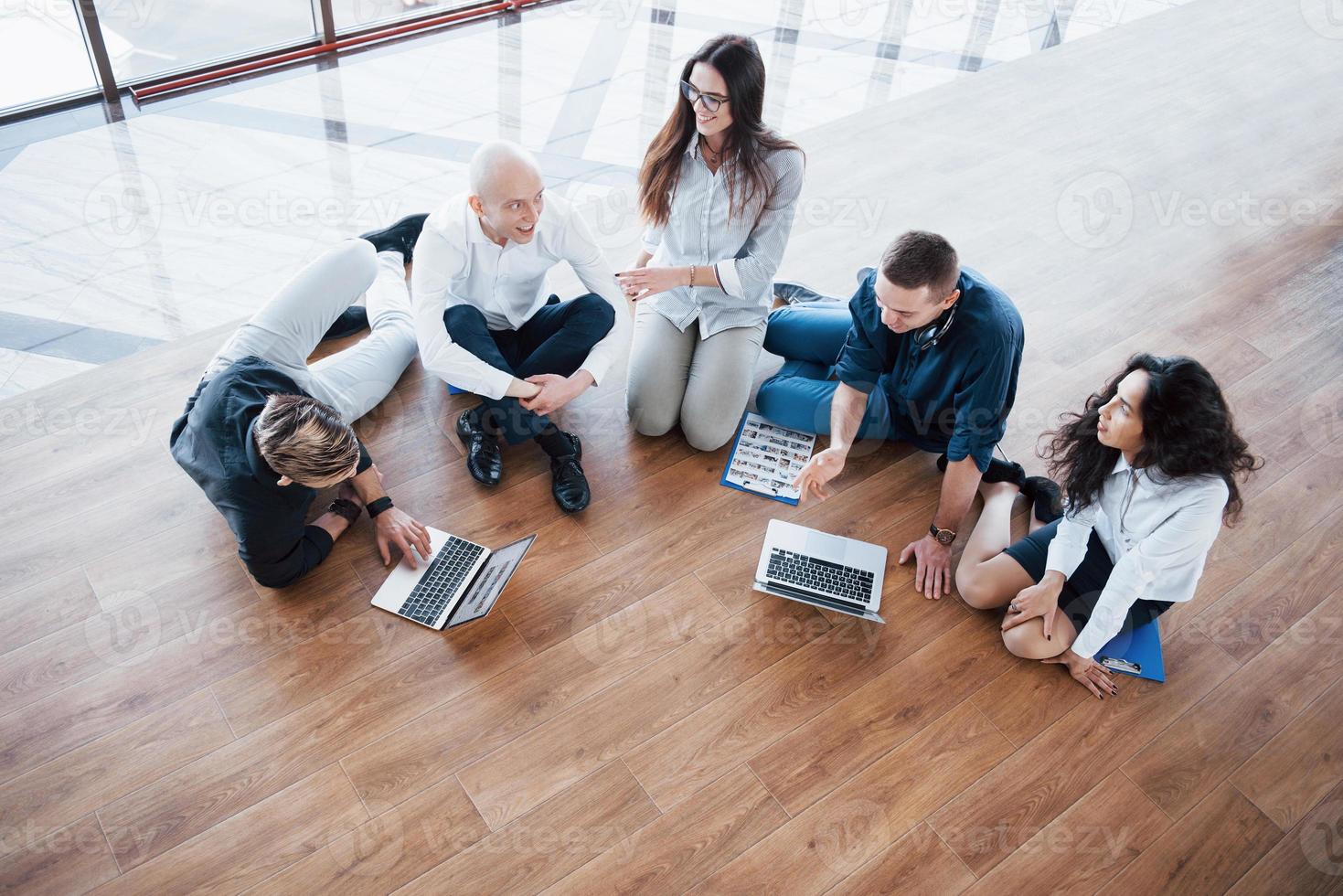Young creative people in modern office. Group of young business people are working together with laptop. Freelancers sitting on the floor. Cooperation corporate achievement. Teamwork concept photo