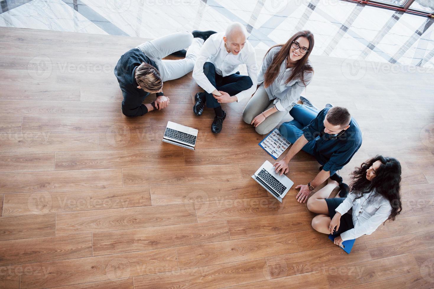 Young creative people in modern office. Group of young business people are working together with laptop. Freelancers sitting on the floor. Cooperation corporate achievement. Teamwork concept photo