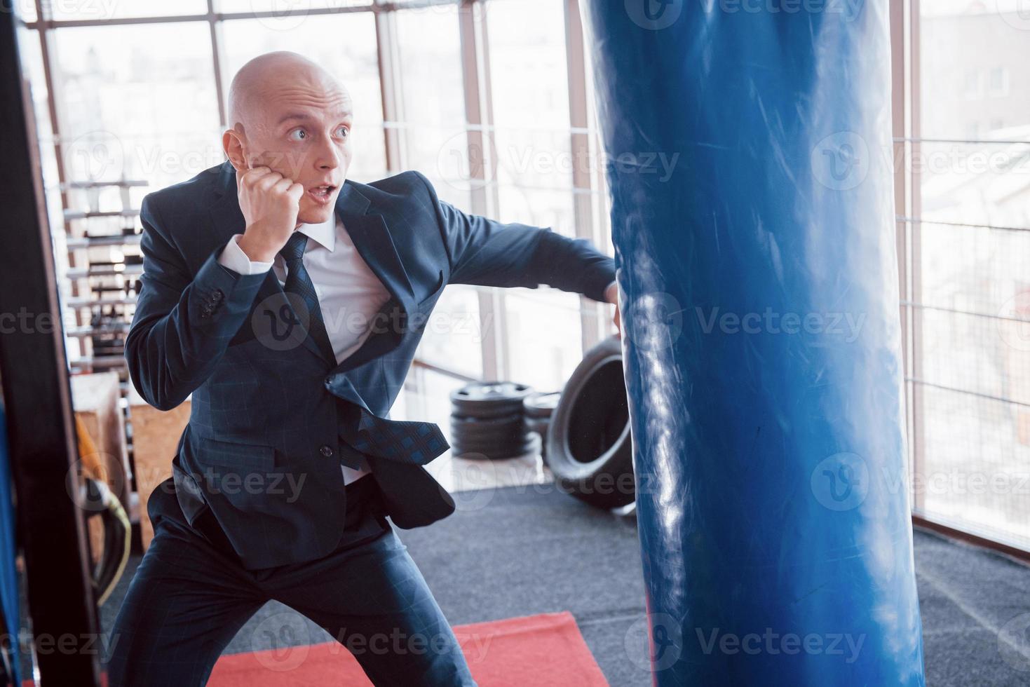 An angry bald businessman beats a boxing pear in the gym. concept of anger management photo