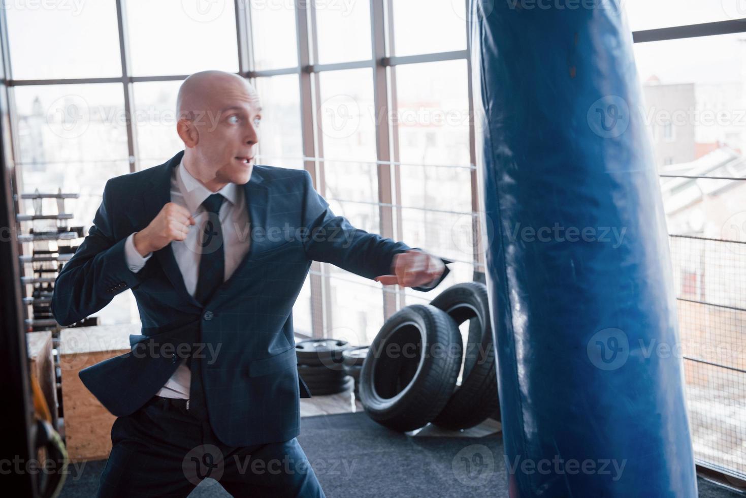 An angry bald businessman beats a boxing pear in the gym. concept of anger management photo