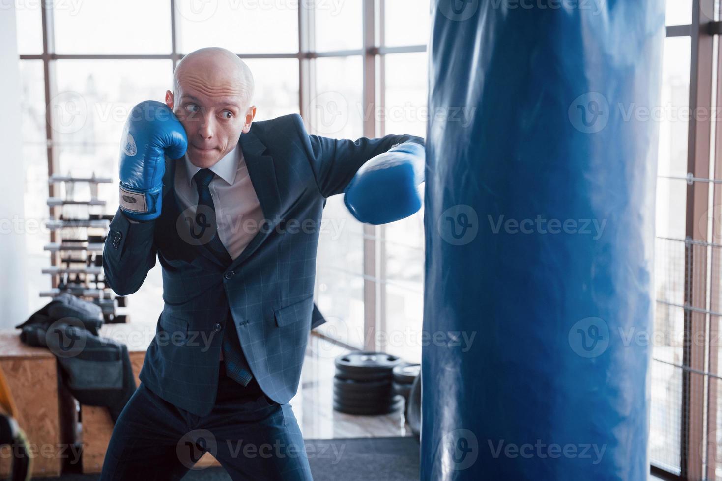 An angry bald businessman beats a boxing pear in the gym. concept of anger management photo