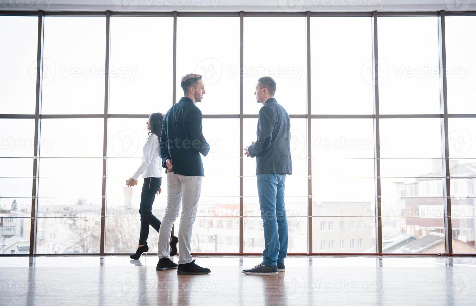 Two businessmen deep in discussion together while standing in an office boardroom with windows overlooking the city photo