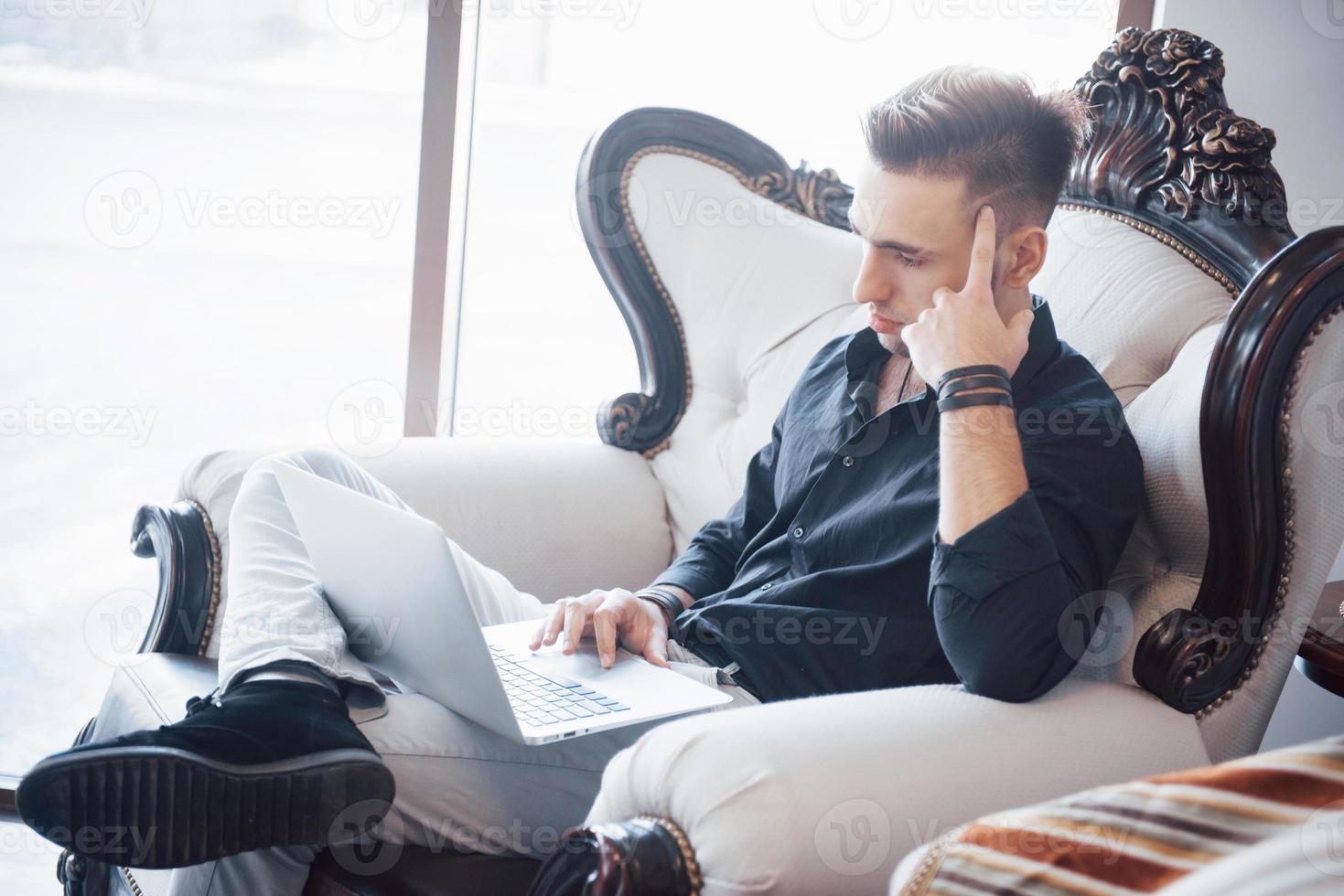 young businessman working on modern loft office. Man wearing white shirt and using contemporary laptop. Panoramic windows background. photo