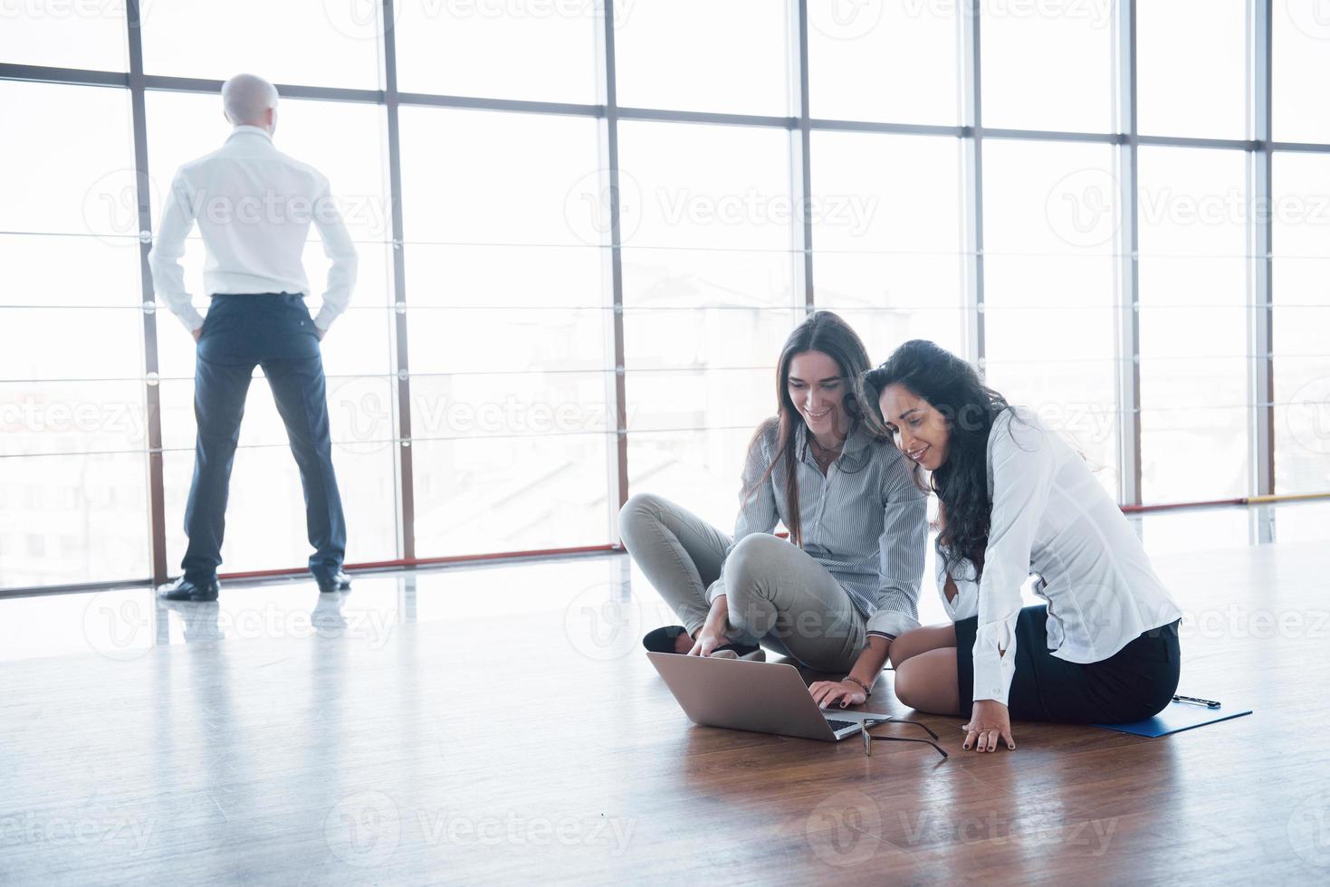 Young creative people in modern office. Group of young business people are working together with laptop. Freelancers sitting on the floor. Cooperation corporate achievement. Teamwork concept photo