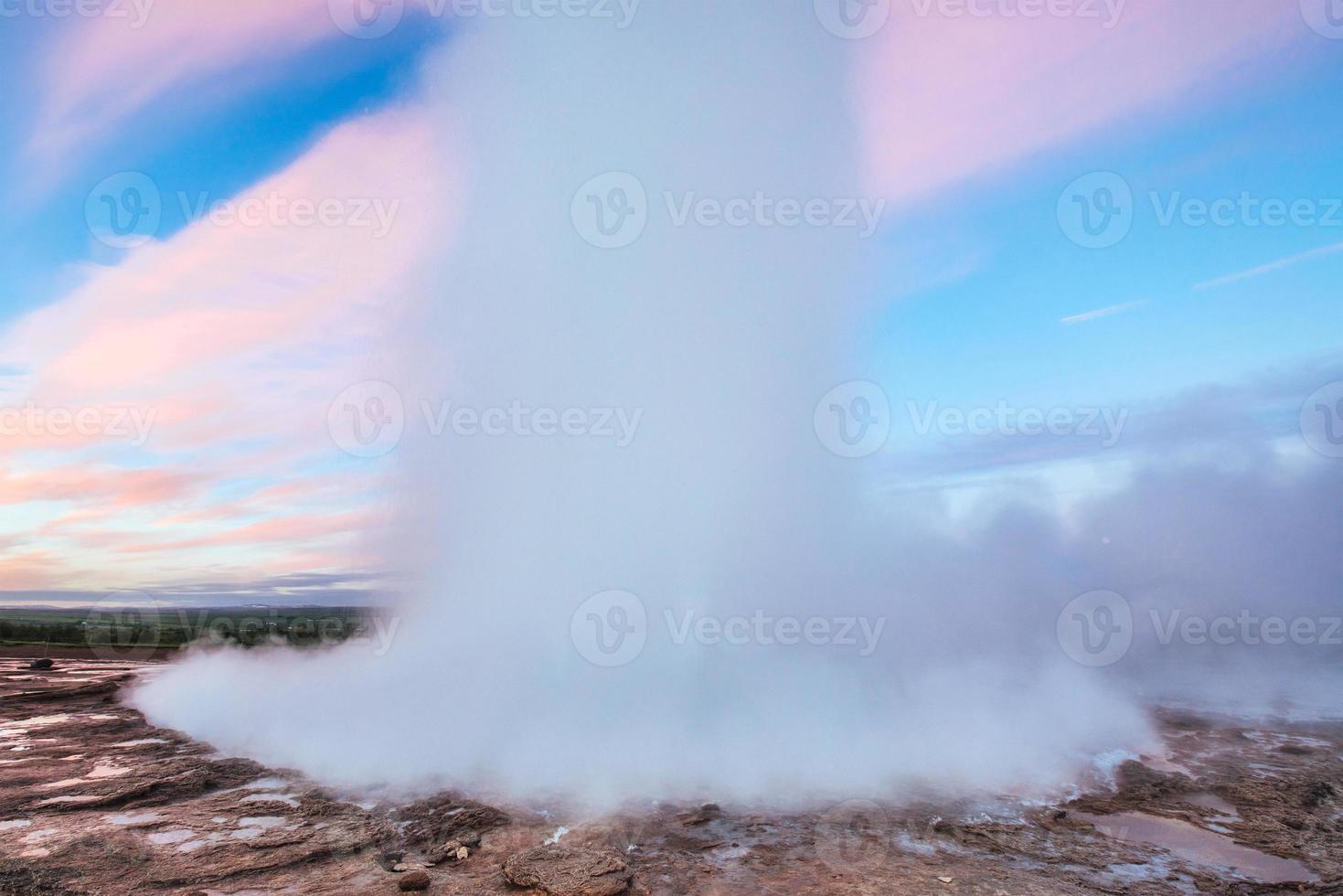 Strokkur geyser eruption in Iceland. Fantastic colors shine through the steam. Beautiful pink clouds in a blue sky photo