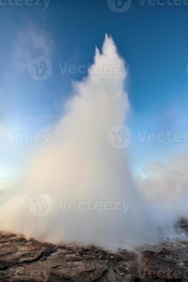 Strokkur geyser eruption in Iceland. Fantastic colors shine through the steam. Beautiful pink clouds in a blue sky photo