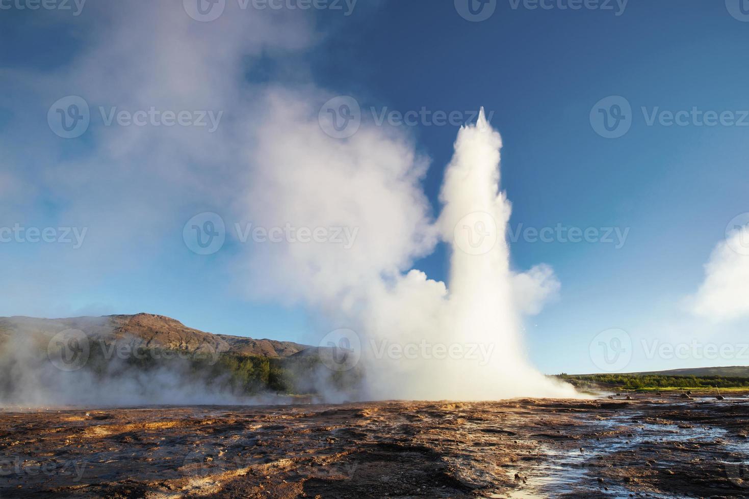 Erupción del géiser strokkur en islandia. colores fantásticos brillan a través del vapor. hermosas nubes rosadas en un cielo azul foto