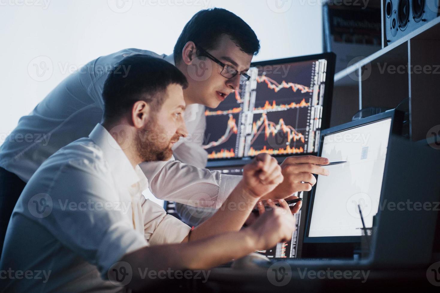 Team of stockbrokers are having a conversation in a dark office with display screens. Analyzing data, graphs and reports for investment purposes. Creative teamwork traders photo