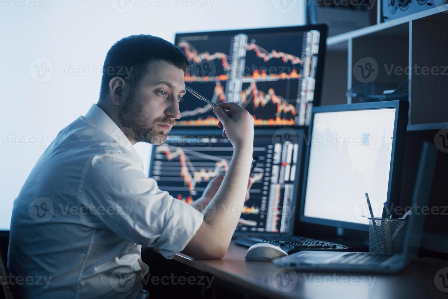 Stressful day at the office. Young businessman holding hands on his face while sitting at the desk in creative office. Stock Exchange Trading Forex Finance Graphic Concept photo