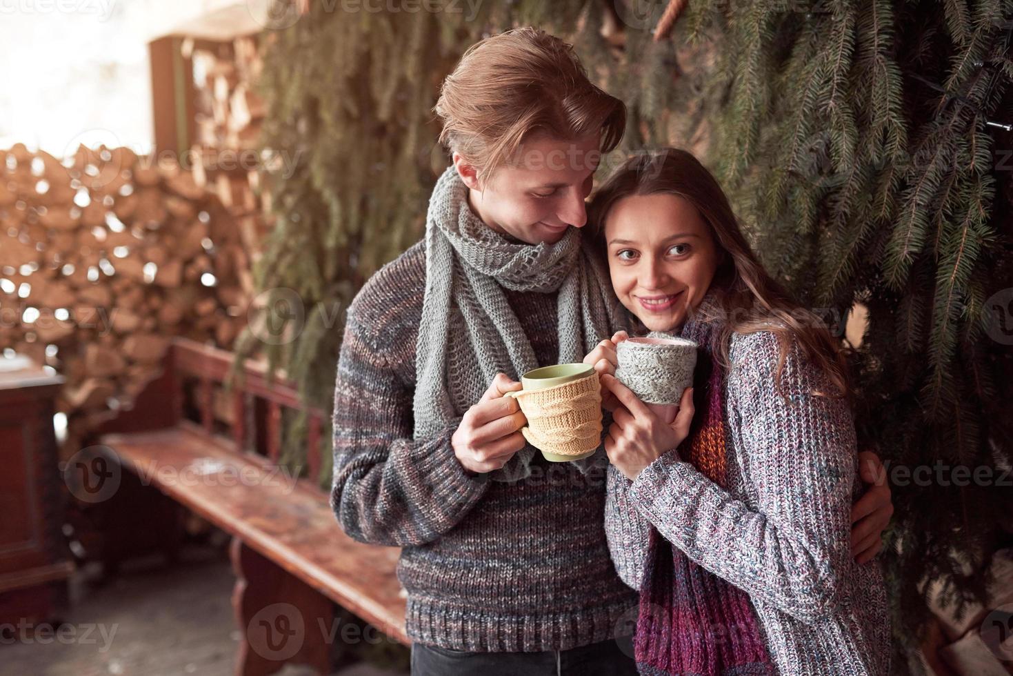 Photo of happy man and pretty woman with cups outdoor in winter. Winter holiday and vacation. Christmas couple of happy man and woman drink hot wine. Couple in love