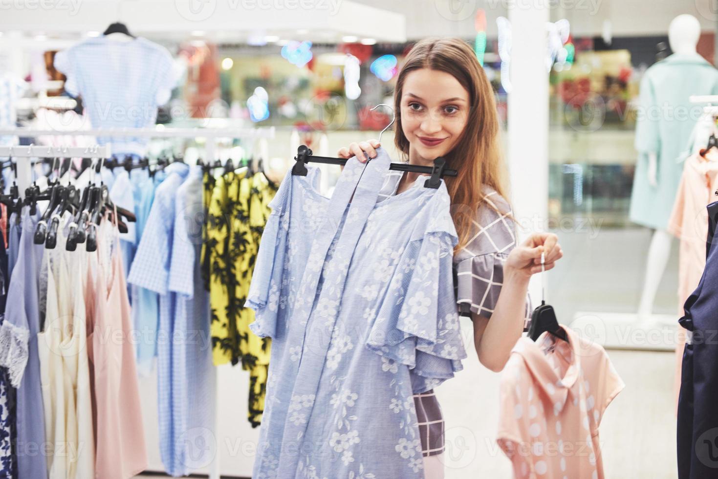 concepto de venta, moda, consumismo y personas - mujer joven feliz con bolsas de compras eligiendo ropa en el centro comercial o tienda de ropa foto