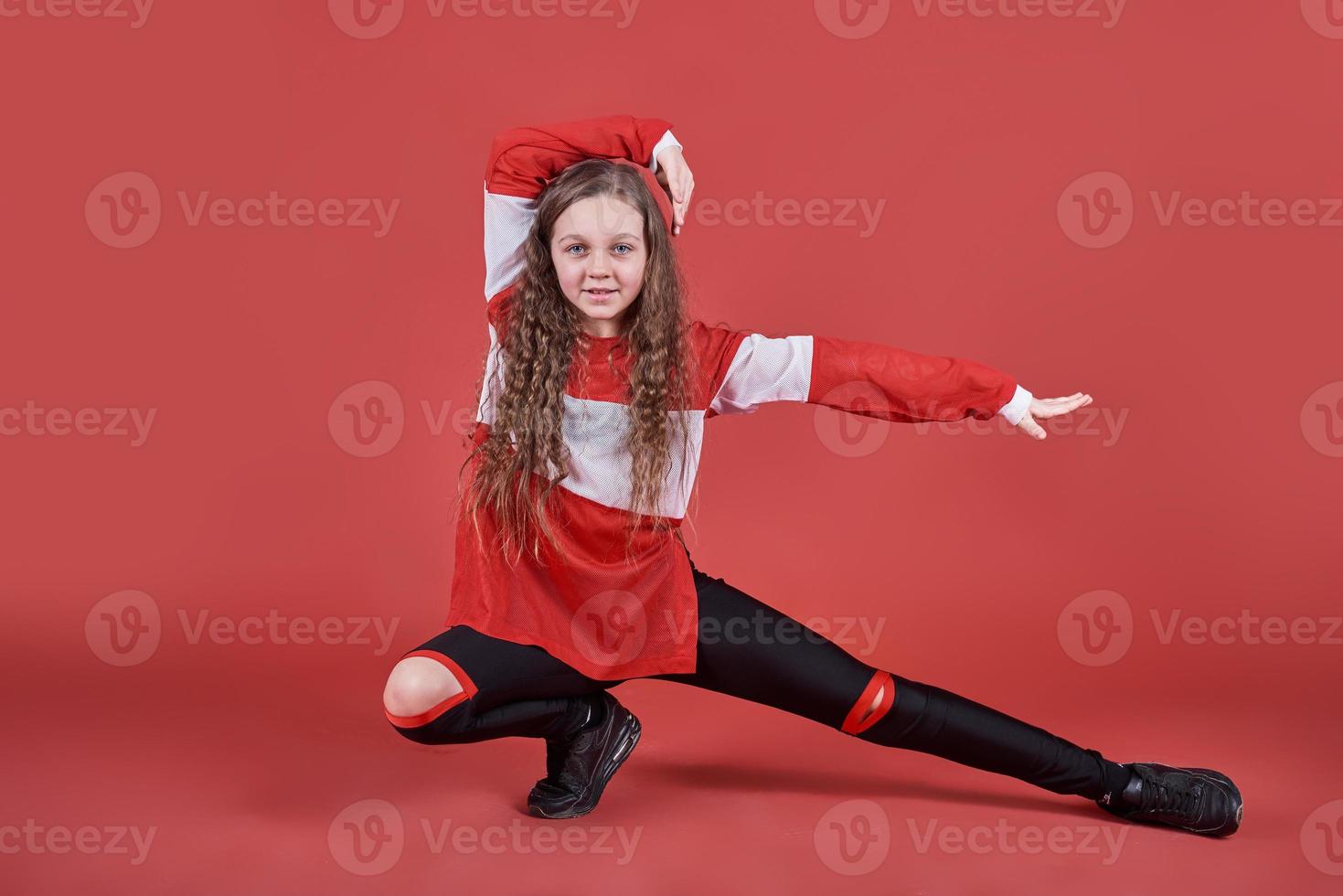Young urban woman dancing on red background, modern slim hip-hop style teenage girl photo